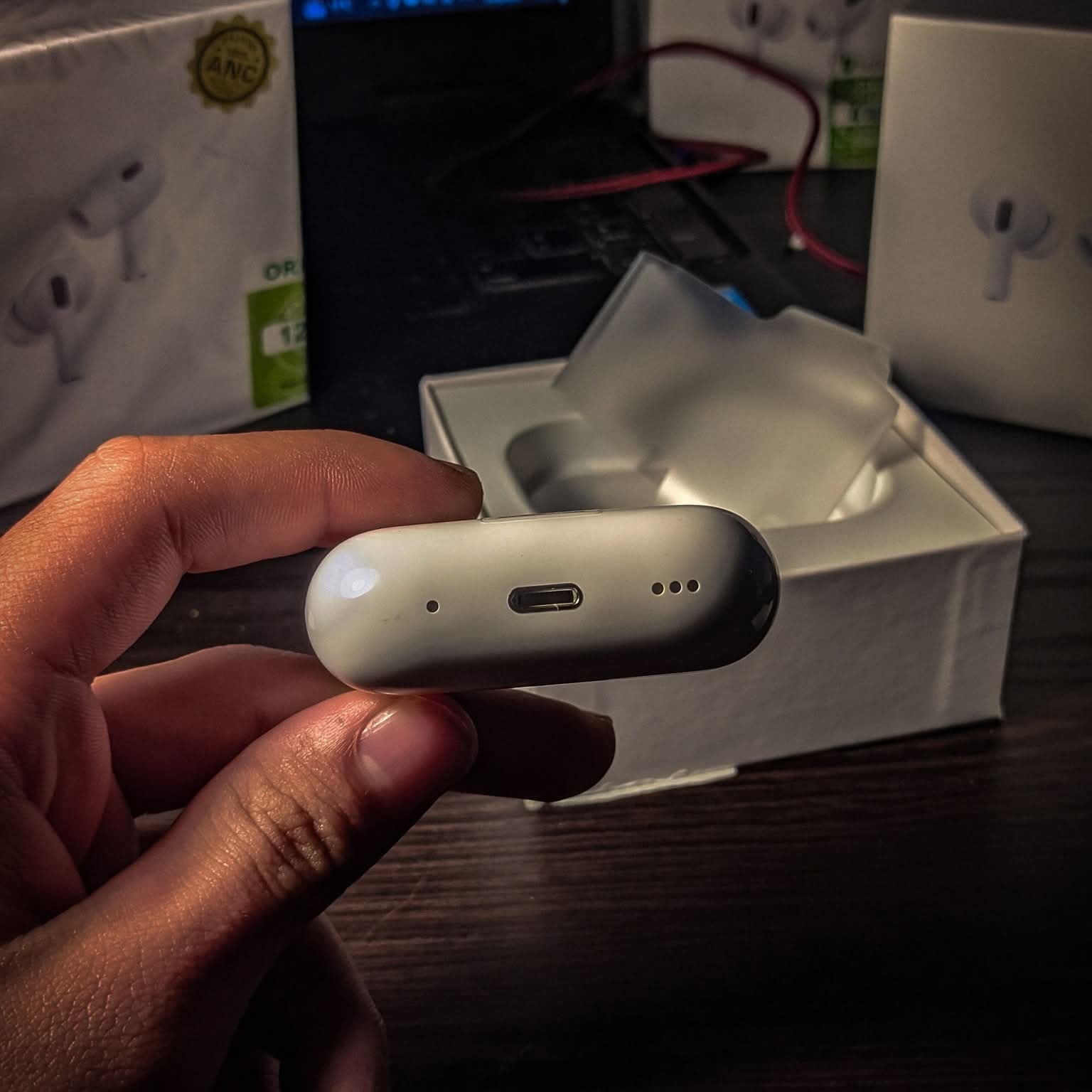 Hand holding a small electronic device with a blurred background of tech products.